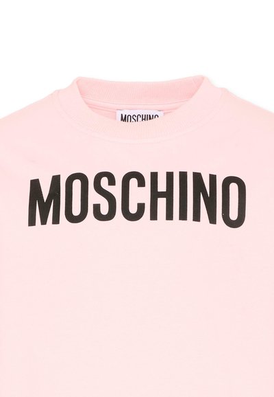 Jasnoróżowa bluza z okrągłym dekoltem, z wyraźnym czarnym logo MOSCHINO na wysokości klatki piersiowej.