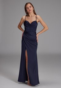 Robe de soirée en satin marine avec un décolleté drapé, un corsage ajusté et une fente sur le côté. Présente des bretelles fines et une jupe fluide.
