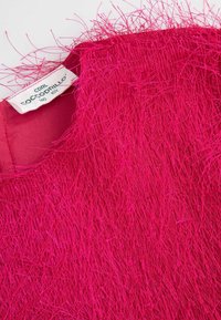 Tkanina w kolorze fuksji o fakturze z długimi, luźnymi nitkami. Ubranie ma okrągły dekolt i wewnętrzną metkę pielęgnacyjną.