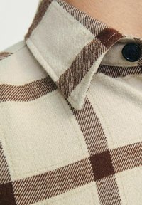 Chemise en flanelle beige à motif vichy brun, dotée d'un col à boutons et d'un tissu doux et texturé.