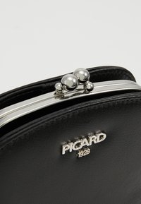 Portefeuille en cuir noir avec fermoir en métal argenté, présentant trois accents arrondis et le logo embossé "PICARD 1928" à l'avant.