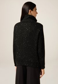 Schwarzer gerippter Pullover mit hohem Kragen, ausgestattet mit einer strukturierten Strickware und verstreuten metallischen Verzierungen für einen dezenten Glanz.