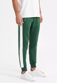 Gröna sportbyxor med ett vitt sidostreck, joggerstil, tillverkade av slät väv. Matchade med vita sneakers, smal passform vid anklarna.