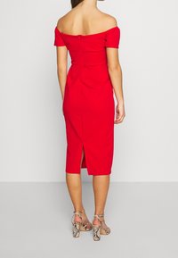Robe rouge décolletée avec un design ajusté, longueur genou, fermeture éclair au dos et fente à l'arrière. Associée à des sandales à talons en imprimé serpent.