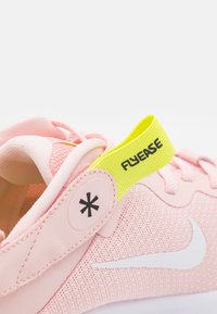 Sneaker in tessuto rosa con swoosh Nike bianco, tomaia strutturata e linguetta gialla con la scritta "FLYEASE". Accento circolare nero vicino al tallone.