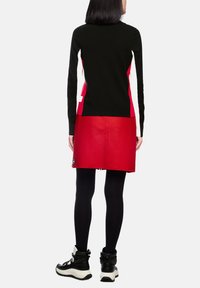 Schwarz-rotfarbiges, farblich abgesetztes Kleid mit langen Ärmeln, glatter Textur und Logodetail am Saum. Kombiniert mit schwarzen Leggings und Stiefeln.