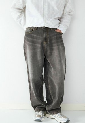 Grau-Jeans aus Denim mit lockerem Schnitt, einer ausgebleichten Textur und kontrastierenden gelben Nähten. Kombiniert mit hellgrauen Sneakers.