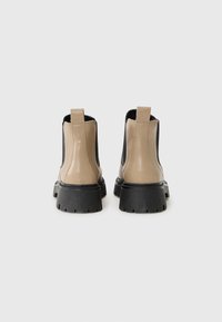 Botines beige y negros hechos de material sintético suave, con una suela gruesa negra y lengüetas para facilitar su uso.