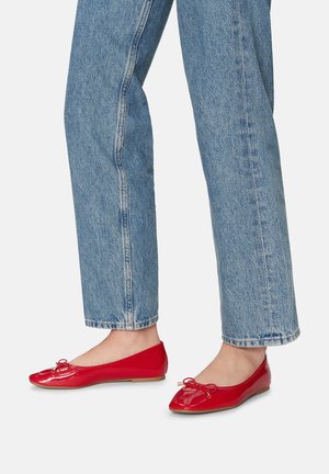 Czerwone lakierowane baletki na niskim obcasie, z kokardką na czubku i gładką, błyszczącą teksturą. Połączone z jasnoniebieskimi, wyblakłymi dżinsami.