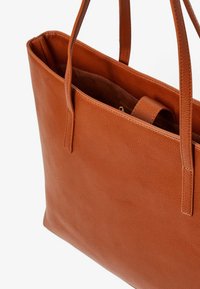 Brown leather tote bag with two long handles, rectangular shape, smooth texture, and a large main compartment for storage.