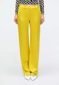 Pantalones anchos de pierna ancha en color amarillo con una textura suave y presillas para cinturón. Combinados con tacones blancos de punta puntiaguda para contraste.