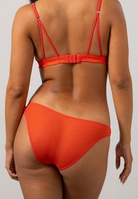 Set di lingerie rossa con vista posteriore. Il reggiseno ha spalline regolabili e chiusura a gancio; le mutandine sono a vita bassa con copertura minima.