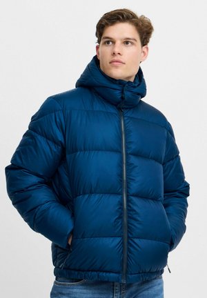 Marineblå pufferjakke med høy krage og glidelåslukking. Har et quiltet design og to sidelommer.