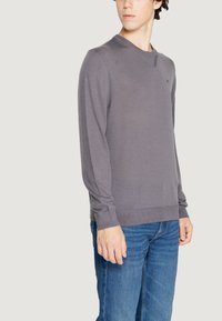 Maglione grigio a maniche lunghe con scollo rotondo, realizzato in materiale knit leggero. Presenta polsini e orlo a costine, e un sottile dettaglio del logo.