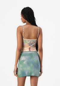 Uzorasti crop top s tankim trakama; ima šarene cvjetne i umjetničke uzorke. Dodaje mu se sjajna mini suknja u zelenkasto-plavoj boji.