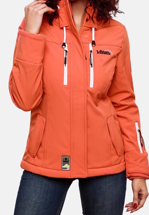 Kvinde iført en orange softshell-jakke med lynlåse foran og på ærmerne, hvide snore og bjerglogo, kombineret med mørkeblå jeans.