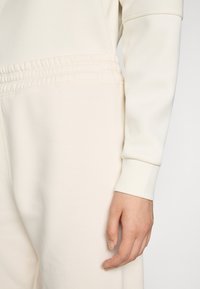 Cream-colored sweatshirt with ribbed cuffs and an elastic waistband. Soft fabric texture visible, showcasing a simple, seamless design.