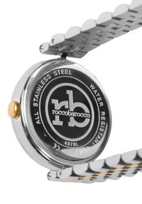 Reloj de acero inoxidable con una esfera negra que incluye el logotipo de la marca, una corona de color dorado y una indicación de resistencia al agua; pulsera metálica vinculada.