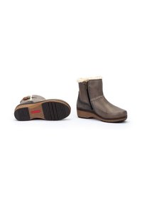 Bottines en cuir marron avec doublure en fausse fourrure, fermeture éclair latérale, semelle texturée et un léger talon compensé. Présente un détail de couture décoratif.