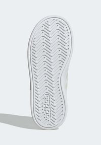 Bílá podrážka z gumy na tenisku s rybí kostrou, vyraženým logem značky a zelenými akcenty po stranách.