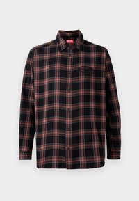 Camicia a quadri nera e rossa con chiusura a bottoni, maniche lunghe e un'etichetta sul colletto. Presenta cuciture a contrasto e una tasca a pattina.