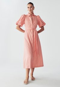 Roza, midi haljina kratkih rukava s dugmadi sprijeda, strukirana s pojasom. Glatka tekstura, opušteni kroj i blago napuhane rukave.