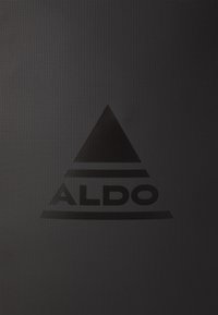 Černé texturované pozadí s výrazným černým trojúhelníkovým logem pod nímž je text "ALDO". Jednoduché a moderní designové prvky.