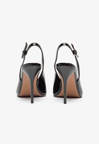 Μαύρες πατέντα δερμάτινες σάνταλες με τακούνι, με κομψό σχέδιο, ανοιχτή πλάτη, λουράκι στον αστράγαλο και λεπτό τακούνι στιλέτο. Υφή στη σόλα και ελάχιστες λεπτομέρειες.