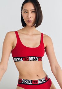 Rdeča bombažna bralette in bikiniji, ki vključuje črn elastični pas z belim in rdečim logotipom "DIESEL". Gladka tekstura, športen dizajn.
