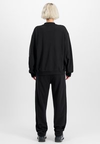 Crni oversized dukserica i odgovarajuće trenirke, napravljene od mekanog materijala, sa opuštenim krojem, rebrastim manžetama i minimalističkim dizajnom.