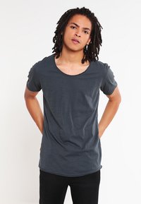 T-shirt droit gris foncé à manches courtes avec un col rond, présentant une texture douce et une coupe décontractée. Porté sur un pantalon noir.
