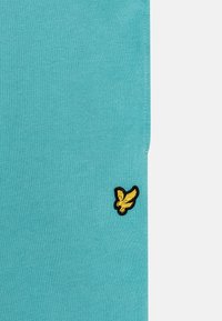 Maglione turchese con una texture a coste, caratterizzato da un piccolo logo ricamato di un uccello nero e giallo sul lato sinistro.