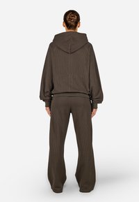 Brązowa, prążkowana bluza z kapturem oraz dopasowane spodnie z szerokimi nogawkami, posiadające kaptur, długie rękawy i teksturowany materiał. Brak widocznych logo lub wzorów.