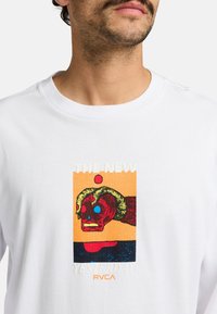 White cotton t-shirt featuring a colorful graphic print with a red skull, yellow and blue accents, and text reading "THE NEW YESTERDAY RVCA."