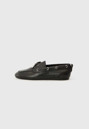 Chaussures bateau en cuir noir avec bout arrondi, devant à lacets, oeillets en métal et semelle plate. Elles sont dotées d'une petite languette à l'arrière.
