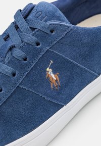 Niebieskie zamszowe sneakersy z tonalnym przeszyciem, białą gumową podeszwą i haftowanym brązowym logo polo. Posiadają płaskie sznurowadła oraz gładkie wewnętrzne wykończenie.
