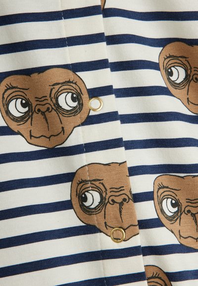 Stripet stof med marineblå og creme farver, der har gentagne brune alien ansigt illustrationer; inkluderer en guldfarvet øjer detalje.