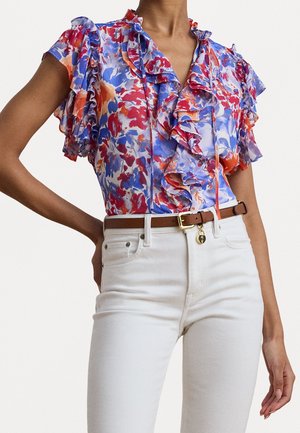 Květovaná halenka s volány v červené, modré a oranžové barvě s krátkými zvonovými rukávy, kombinovaná s bílými džínami s vysokým pasem a hnědým koženým pásem se zlatou sponou.