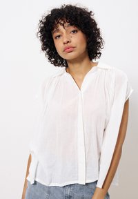 Weißes, leichtes Blusenshirt mit kurzen Ärmeln, knopflosem Vorderteil und subtiler Glanzoptik, das einen lässigen Schnitt und eine weiche Textur aufweist.