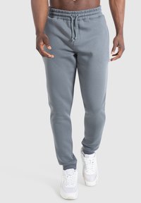 Pantalones deportivos grises con cintura elástica y cordón ajustable. Tejido suave y diseño de pierna cónica. Combinados con zapatillas blancas.