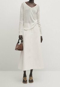 Lekki, dziany biały sweter z dekoltem w serek, w połączeniu z kremową spódnicą do kostek. Brązowa torebka i sandały w dwóch kolorach dopełniają całość.
