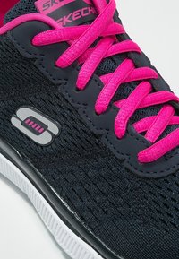 Sneakers Skechers z teksturowanym czarnym materiałem z siateczki, jasnoróżowymi sznurówkami oraz białą gumową podeszwą z logo po boku.