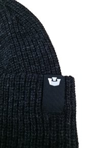 Beanie nero a maglia con un motivo testurizzato, dotato di un'etichetta rettangolare nera con un logo bianco sul lato.