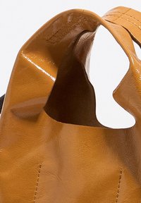 Koniakowa torba z faux skóry o gładkiej, błyszczącej powierzchni i wyciętymi uchwytami. Posiada starannie wyszywane akcenty oraz fakturowane wnętrze.