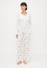 Bela dolga majica z dolgimi rokavi in gumbi; ohlapne, patterned pižamne hlače z jelenčki in cvetlicami v mehkih pastelnih barvah.