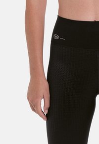 Black high-waisted active leggings with a textured pattern, featuring a smooth waistband and a small branding logo on the front.