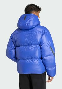 Modrá prešívaná bunda s kapucňou, s lesklým povrchom, prešívaným dizajnom a šedými akcentmi na rukávoch. Ľahká a zateplená.