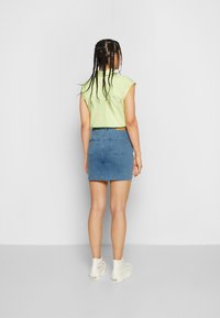 Camisa verde claro de mangas curtas, saia de ganga azul com a barra desfiada e ténis brancos de plataforma. Cabelo estilizado em tranças.