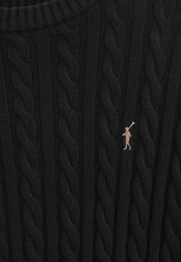 Svart kabelstickad tröja med ribbad halsringning, med en liten, broderad logotyp i en kontrasterande färg på bröstet.