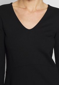 Black long-sleeve top featuring a deep V-neck, fitted bodice, and smooth texture, with an empire waist seam detail.